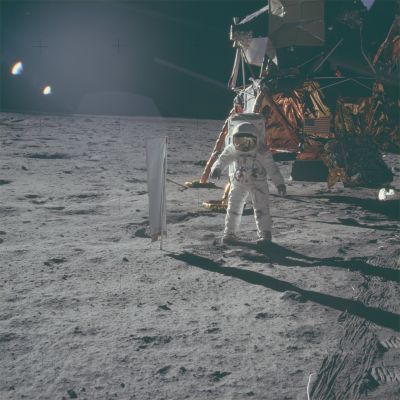 AS 11-40-5873 - Aldrin near the Solar Wind Collector
Caption NASA originale:"Neil took this picture of Buzz at about 110:03:24. Buzz has just deployed the Solar Wind Collector (SWC). Neil took the photo toward the southeast. Buzz is standing flat-footed next to the SWC, facing Neil, who is at about the 2 o'clock position out from the LM. In the lower right corner, notice the scratch marks that the TV cable made as Neil pulled it out. The multiple tracks were made by the individual cable loops scraping along the ground. We can see underneath the engine bell. Most of the surface in this image has not been disturbed as yet, and in the places where Neil and Buzz have walked, the disturbed surface is darker. Good illustration of this very common phenomenon. Jack Schmitt speculates that the Descent Engine plume swept away the smallest particles, leaving a higher than normal percentage of larger particles. The more jagged surface is a better reflector of sunlight than the normal surface and, therefore, appears brighter. Certainly, from orbit, the areas around the landed LM's are brighter than the normal surface. As they walk around, the astronauts disturb this modified surface and, in effect, restore it's normal condition. We see the MESA, in shadow, to the right of Buzz. On the front of Buzz's suit, we have the RCU, the camera bracket, and just above his crotch, the "Red Apple" activator for the purge valve. He has some dirt on his knees. A detail shows a carabiner fitted to the end of his neckring tiedown".
Parole chiave: Lunar Equipment - SWC