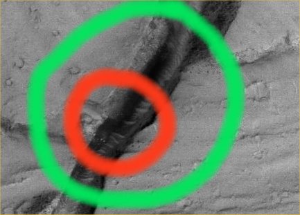 Features of Cerberus Fossae (Original NASA/MGS/MSSS EDM b/w Frame) 
Cerchiatura Rossa: presenza di un gruppo di almeno cinque corpuscoli puntiformi (rocce cristalline?) i quali, pur essendo in ombra, appaiono decisamente molto luminosi.
Si nota inoltre, proprio al centro della Cerchiatura Rossa, la presenza di un rilievo scuro (un altro "seep" oppure un'ombra vera e propria?) i cui contorni, tuttavia, sembrano troppo netti per farci pensare ad un rilievo  naturale (non pensiamo ad una manipolazione digitale bensì, piuttosto, ad un rilievo troppo complesso da potersi vedere chiaramente ad una risoluzione che, pur se buona, è ancora troppo bassa per consentire la visione accurata di profili particolarmente intricati come potrebbe essere quello in questione).
Parole chiave: Mars from orbit - Channels - Cerberus Fossae Region