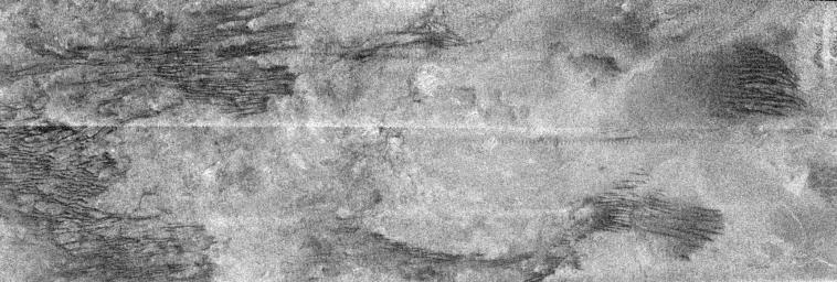 Channels on Titan or just Windstreaks?
Caption NASA originale:"Running across the image (about 300 Km across) are a series of roughly parallel, mostly east-west dark linear features that join and separate, which are not seen in the previous radar images. They may be formed by the action of eastward-flowing winds, or geologic processes acting on the crust itself. In places they cut through adjacent terrain, while elsewhere the lineaments seem to be interrupted by brighter material, appearing again on the other side. Seams between radar segments are visible as horizontal, sawtooth-shaped lines. Bright material in radar images may be rough or sloped toward the radar (which is observing from the top in this frame). Also, some of what is seen may in fact be below the surface, revealed as the radio waves penetrate overlying, radar-transparent material".
Parole chiave: Saturn's Moons - Titan