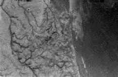 Shoreline and Drainage Channels' Network on Titan 
Caption ESA originale:"This is one of the first raw images returned by the ESA Huygens probe during its successful descent. It was taken from an altitude of 16,2 Km with a resolution of approximately 40 metres per pixel. It apparently shows short, stubby drainage channels leading to a shoreline".
Il profilo di un tratto costiero, dunque: montagne (o colline), una fitta rete di canali ed una porzione di "mare" alla vista. Mare.
Già, ma un mare fatto di cosa?...
Parole chiave: Titan's surface