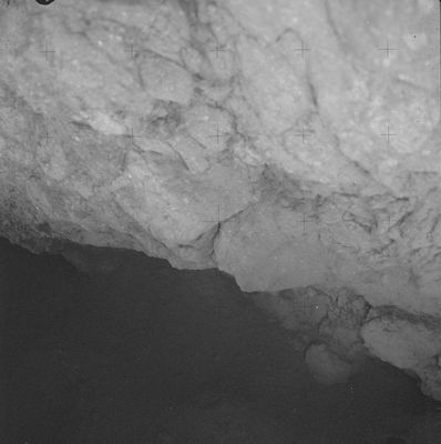 AS 16-106-17411 - In the eternal shadows... (4) - HR
Versione a contrasti esaltati ("enhanced") del frame precedente. Purtroppo, nonostante gli sforzi, non riusciamo a vedere molto di quello che si cela al di sotto di Shadow Rock, ma le forme che cogliamo e che giacciono nella penombra ci fanno istintivamente venire in mente una roccia di origine ignea, ma dai profili smussati. 

Così smussati ed addolciti da renderla, nel suo genere, se non unica, quantomeno molto rara. 
Non si colgono, neppure operando notevoli ingrandimenti, riflessi indicativi della presenza, nel suo tessuto, di microcristalli - come quelli che riscontriamo nei graniti -; in compenso si vedono una serie di curiosi rigonfiamenti ed increspature i/le quali fanno pensare all'azione di agenti diversi ed ulteriori sia alle alte temperature (e dunque, se questa roccia è una varietà di basalto, essa dovrebbe aver subìto, nelle ere, un intenso e prolungato "weathering"), sia al gelo estremo della notte lunare.

Conclusioni (perdonateci, ma) non è possibile trarne; tuttavia, sul fatto che Shadow Rock, prima di giacere là dove adesso la vediamo (e dove pensiamo giaccia tutt'ora), si trovasse in un ambiente geologicamente (e forse non solo geologicamente...) "vivo", a noi non sembra un'eventualità da gettare via aprioristicamente e con leggerezza...
Parole chiave: Lunar Surface - under Shadow Rock