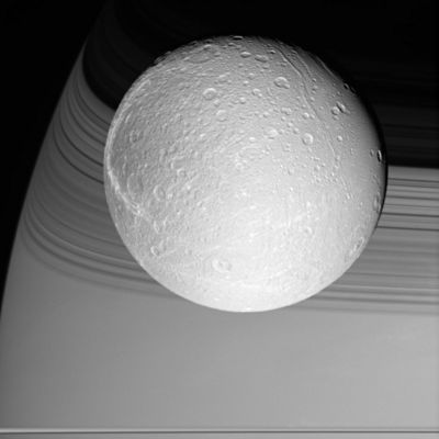 Dione: over the clouds of Saturn
Original caption:"Cassini prepared for its rendezvous with Dione on Oct. 11, 2005, capturing the brilliant, cratered iceball in front of its shadow-draped planet. The terrain seen here becomes notably darker toward the West, and is crosscut by the bright, fresh canyons that form wispy markings on Dione's Trailing Hemisphere. 

The image was taken in visible light with the Cassini wide-angle camera at a distance of approx. 24.500 Km (about 15.200 miles) from Dione and at a phase angle of 22°. The image scale is about 2 Km (about 1 mile) per pixel".
Parole chiave: Saturn's Moons - Dione