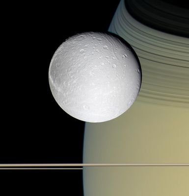Dione and Saturn (natural colors)
Original caption:"Speeding toward pale, icy Dione, Cassini's view is enriched by the tranquil gold and blue hues of Saturn in the distance. The horizontal stripes near the bottom of the image are Saturn's Rings. The spacecraft was nearly in the plane of the Rings when the images were taken, thinning them by perspective and masking their awesome scale. The thin, curving shadows of the C-Ring and part of the B-Ring adorn the Northern Latitudes visible here, a reminder of the Rings' grandeur. 
It is notable that Dione, like most of the other icy Saturnian satellites, looks no different in natural color than in monochrome images. Images taken on Oct. 11, 2005, with blue, green and infrared (centered at 752 nnmts) spectral filters were used to create this color view, which approximates the scene as it would appear to the human eye. The images were obtained with the Cassini spacecraft wide-angle camera at a distance of approx. 39.000 Km from Dione and at a phase angle of 22°.
The image scale is about 2 Km/pixel".
Parole chiave: Saturn's Moons - Dione