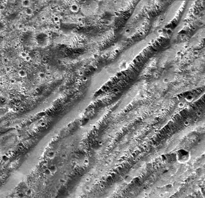 Scarps on Ganymede
Original caption:"NASA's Galileo spacecraft took this image of dark terrain within Nicholson Regio, near the border with Harpagia Sulcus on Jupiter's moon Ganymede. The ancient, heavily cratered dark terrain is faulted by a series of scarps. The faulted blocks form a series of "stair-steps" like a tilted stack of books. On Earth, similar types of features form when tectonic faulting breaks the crust and the intervening blocks are pulled apart and rotate. This image supports the notion that the boundary between bright and dark terrain is created by that type of extensional faulting.
North is to the right of the picture and the Sun illuminates the surface from the west (top). The image is centered at -14° latitude and 320°  longitude and covers an area approx. 16 by 15 Km (about 10 by 9 miles). The resolution is 20 mt (66 feet) per picture element. The image was taken on May 20, 2000, at a range of 2.090 Km (about 1.299 miles)".
Parole chiave: Jupiter Moons - Ganymede