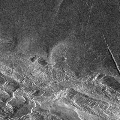 Magellan Probe: radio image of Lakhsmi Planum and Danu Montes
Caption NASA originale:"Southwest Lakshmi Planum is bounded on the south by the Danu Montes. Lakshmi Planum is an elevated plateau that is bounded on all sides by mountain chains. Here, the Danu mountains have an angular fractured appearance. Chasms slice diagonally across the mountains in the lower left (southwest) corner of the image. Because of the steep slopes and the local relief of the mountains of several kilometers, these fault-bounded troughs appear to zig-zag through the mountains when, in fact, they are probably straight if viewed from above. The radar view provides a perspective that would place the viewer's eye to the right, 27° above the horizon. Thus, slopes facing to the right can be seen completely, though dark, and slopes facing away to the left appear shortened, often seen only as thin bright lines. In the center of the image is a low volcanic dome 20 Km in diameter. This type of volcanic feature frequently occurs on the low plains. This dome on the edge of Lakshmi is deformed and faulted where it has been affected by the forces that created the Danu mountains".
Parole chiave: Naked Venus