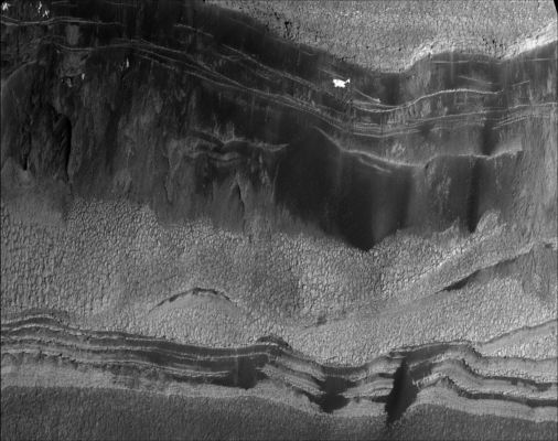 The Walls of Chasma Boreale
The Martian terrain in this remarkable image is at the head of a large chasm, named Chasma Boreale, which cuts through Mars' North Polar Layered Deposits (MNPLD). These ice-rich layered deposits are about 3000 mt (about 9.800 feet) thick and 1000 Km (1.600 miles) across, much like the Greenland ice-sheet on Earth. The head of Chasma Boreale ends in a steep icy cliff more than 1000 mt (about 3300 feet) high. The cliff has both light- and dark-toned layers, seen at right in this image. The image was taken by the HiRISE camera on NASA's MRO. The internal layers of the ice-sheet are visible in the cliff walls. The dark-toned flat area in the center and left of the image is the floor of this chasm, which contains many craters.
Scientists have proposed that Chasma Boreale was formed by a catastrophic flood that began under the ice-sheet and was later widened by wind erosion. However, the large number of craters on the chasm's floor implies that the floor is much older than the ice sheet. These craters should have been removed by the suggested flood; their presence has caused some Mars researchers to instead speculate that no large flood occurred and that Chasma Boreale was not covered with very much ice. 

In addition to layered ice, there is also some material within the north polar layered deposits that appears to be composed of sand. The dark material near the base of the cliff wall is thought to be aprons of debris being eroded from sand-rich layers. Zooming in on this dark material with HiRISE reveals ripples, which are diagnostic of moving sand. 

Some bright spots of material visible on the cliff wall were not present in previous years. These are likely patches of water frost. Each year layers of carbon dioxide and water frost coat this terrain before being removed during the summer. The water frost lasts longer, and patches that are shaded by nearby steep topography (such as this one) can persist even into late summer. 

An unexpected surprise, not visible with previous camera resolutions, is the fragmentation of the exposed surfaces of these icy layers into polygonal blocks. These blocks appear to be breaking away from the layer margins and forming boulder-sized debris, which then rolls down slope (a process called mass-wasting). These boulders are likely to be large blocks of dusty water ice; once separated from the main ice-sheet they can be eroded away by sunlight. More boulder-sized objects are visible out in the floor of the chasm. Polygons are also visible throughout the chasm floor, indicating that water-ice is just below the surface. 
Image TRA_000845_2645 was taken by the HiRISE camera on Oct. 1, 2006. The complete image is centered at 84.6 degrees latitude, 3.4 degrees east longitude. The range to the target site was 316 kilometers (198 miles). At this distance the image scale is 63 centimeters (25 inches) per pixel (with 2 x 2 binning), so objects about 186 centimeters (73 inches) across are resolved. The image shown here has been map-projected to 50 centimeters (20 inches) per pixel. North is up. The image was taken at a local Mars time of 3:34 p.m. and the scene is illuminated from the west with a solar incidence angle of 62.3 degrees, thus the sun was about 27.7 degrees above the horizon. At a solar longitude of 114.3 degrees, the season on Mars is northern summer. 
Parole chiave: Mars from orbit - North Polar Features - Chasma Boreale