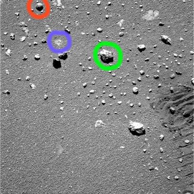 The terrain near Erebus (detail mgnf) - Sol 555
Una possibile risposta - ne siamo certi - potrebbe arrivare dagli Studiosi di Scienze Planetarie e da qualche Geologo un pò "immaginifico": i primi potrebbero - ragionevolmente - ipotizzare che il micro-cratere che vediamo sul fianco della pietra cerchiata in rosso è il prodotto di un evento micro-meteorico (ossìa il buco è il risultato di un "micro-impatto"). 

Qualche Geologo, invece, potrebbe speculare sull'orgine vulcanica della piccola roccia e sui diversi fenomeni che possono produrre la formazione di buchi - o, se si preferisce, di "porosità" - sulle pietre (pensate, p.e., alle "pietre pomici").
Noi, onestamente, non ci sentiamo di esprimere un'opinione "esotica"  riguardo all'origine di questa Singolarità, ma Vi invitiamo a considerare anche questi altri 2 dettagli - forse meno evidenti ma certo non meno importanti: 
Cerchiatura Verde--> c'è una escrescenza di forma circolare sul margine inferiore di quest'altra piccola roccia (è un "berry"?); 
Cerchiatura Blu--> ma cosa c'è sotto i berries?!?
Parole chiave: Mars rocks, sand and debris - Controversial image