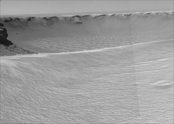 First look inside Victoria Crater (1) - Sol 951
NASA's MER Opportunity reached the rim of Victoria Crater in Mars' Meridiani Planum Region with a 26-mt (85-foot) drive during the Rover's 951st Sol (Sept. 26, 2006). After the drive, the Rover's NavCam took the 3 exposures combined into this view of the crater's interior. This crater has been the mission's long-term destination for the past 21 Earth months. 
A half mile in the distance one can see about 20% of the far side of the crater framed by the rocky cliffs in the foreground to the left and right of the image. The rim of the crater is composed of alternating promontories, rocky points towering approx. 70 mt (230 feet) above the crater floor and recessed alcoves. The bottom of the crater is covered by sand that has been shaped into ripples by the Martian wind. 
The position at the end of the Sol 951 drive is about 6 meters from the lip of an alcove called Duck Bay. The rover team planned a drive for Sol 952 that would move a few more meters forward, plus more imaging of the near and far walls of the crater. 
Parole chiave: Victoria Crater