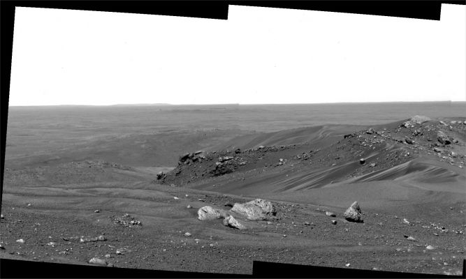 The "Sand-Strewn" Summit of Husband Hill (1) - Sol 603
Original caption:"Undulating bands of dark and light sand, sloping dunes, and scattered cobbles form an apron around a ridge of light-colored rock that stands in bold relief against distant plains, as viewed by NASA's Spirit Rover from the top of Husband Hill on Mars. "The view of the summit is spectacular where we are right now", said geologist Larry Crumpler, with the New Mexico Museum of Natural History and Science, Albuquerque. 

From here, Spirit is looking North-North/East en route to examining more of the local geology of the Columbia Hills in Gusev Crater. A few days after taking this picture, Spirit investigated the small, sinuous drifts on the left, located north-northeast of the rover's position in this image. The last previous time Spirit examined a drift was on the rim of Bonneville Crater almost 500 Soles ago, in March 2004". 
Parole chiave: Mars Panorama - Husband Hill - Summit