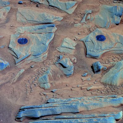 Brushed Rocks on top of Home Plate - Sol 763 (False Colors; credits: NASA/JPL/ASU)
NASA's MER Spirit acquired this false-color image at 11:48 MLST on Mars on the Rover's 746th Sol (such as Feb. 26, 2006), after using the RAT to brush the surfaces of rock targets informally named "Stars" (on the left) and "Crawfords" (on the right). Small streaks of dust extend for several cm behind the small rock chips and pebbles in the dusty, red soils. Because the Rover was looking South-West when this image was taken, the wind streaks indicate that the dominant wind direction was from the South-East. 
The targets Stars and Crawfords are on a rock outcrop located on top of Home Plate. The outcrop is informally named James 'Cool Papa' Bell, after a Negro Leagues Hall of Famer who played for both the Pittsburgh Crawfords and the Kansas City Stars. 

The image combines frames taken by Spirit's PanCam through the camera's 753-, 535- and 432-nnmt filters. It is enhanced to emphasize color differences among the rocks, soils and brushed areas. The blue circular area on the left, Stars, was brushed on 761 (Feb. 22, 2006). The one on the right, Crawfords, was brushed on sol 763 (Feb. 25, 2006).
Parole chiave: Mars rocks, sand and debris - Home Plate Area