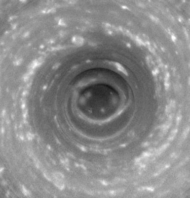 A "Hole" in the (South) "Pole"
Cassini stares deep into the swirling hurricane-like vortex at Saturn's south pole, where the vertical structure of the clouds is highlighted by shadows. Such a storm, with a well-developed eye ringed by towering clouds, is a phenomenon never before seen on another planet. 

This 14-frame movie shows a swirling cloud mass centered on the south pole, around which winds blow at 550 kilometers (350 miles) per hour. The frames have been aligned to make the planet appear stationary, while the sun appears to revolve about the pole in a counterclockwise direction. The clouds inside the dark, inner circle are lower than the surrounding clouds, which cast a shadow that follows the sun. 

At the beginning of the movie, the sun illuminates directly from the top, and by the end it illuminates from the left. The width of the shadow and the height of the sun above the local horizon yield a crude estimate of the height of the surrounding clouds relative to the clouds in the center. The shadow-casting clouds tower 30 to 75 kilometers (20 to 45 miles) above those in the center. This is two to five times greater than the tallest terrestrial thunderstorms and two to five times the height of clouds surrounding the eye of a terrestrial hurricane. Such a height difference arises because Saturn's hydrogen-helium atmosphere is less dense at comparable pressures than Earth's atmosphere, and is therefore more distended in the vertical dimension. 

The south polar storm, which displays two spiral arms of clouds extending from the central ring and spans the dark area inside a thick, brighter ring of clouds, is approximately 8,000 kilometers (5,000 miles) across, which is considerably larger than a terrestrial hurricane. 

Eye-wall clouds are a distinguishing feature of hurricanes on Earth. They form where moist air flows inward across the ocean's surface, rising vertically and releasing a load of precipitation around an interior circular region of descending air, which is the eye itself. 

Though it is uncertain whether moist convection is driving this storm, as is the case with Earthly hurricanes, the dark 'eye' at the pole, the eye-wall clouds and the spiral arms together indicate a hurricane-like system. The distinctive eye-wall clouds especially have not been seen on any planet beyond Earth. Even Jupiter's Great Red Spot, much larger than Saturn's polar storm, has no eye, no eye-wall, and is relatively calm at the center. 

This giant Saturnian storm is apparently different from hurricanes on Earth because it is locked to the pole, does not drift around like terrestrial hurricanes and because it does not form over liquid water oceans. 

The images were acquired over a period of three hours on Oct. 11, 2006, when Cassini was approximately 340,000 kilometers (210,000 miles) from Saturn. Image scale is about 17 kilometers (11 miles) per pixel. The images were taken with the wide-angle camera using a spectral filter sensitive to wavelengths of infrared light centered at 752 nanometers. All frames have been contrast enhanced using digital image processing techniques. The unprocessed images show an oblique view toward the pole, and have been reprojected to show the planet from a perspective directly over the south pole.

Parole chiave: Saturn - Upper Atmosphere - South Pole