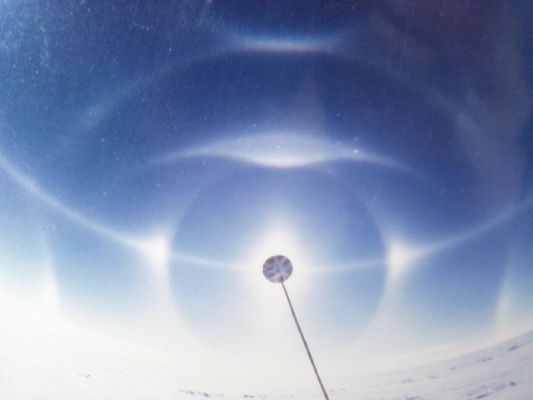 South Polar Halo
When Sunlight reflects and refracts off of tiny ice crystals in the atmosphere, the result can be ice crystal halos, which are related to rainbows (the latter being produced when Sunlight reflects and refracts from water droplets).  
In Antarctica the temperatures are cold and the air is dry, so snow crystals grow very slowly.  This slow growth tends to produce very clean hexagonal prisms, which are well suited for producing beautiful atmospheric displays.  The example here is a South Pole halo, showing a rich variety of arcs and halos.
Halos arise from the way minute ice crystals in the atmosphere scatter Sunlight (or Moonlight!) into different angles.  
The quality of a halo depends on the type and quality of the ice crystals that produce it.  
Parole chiave: Atmospheric Phenomoena