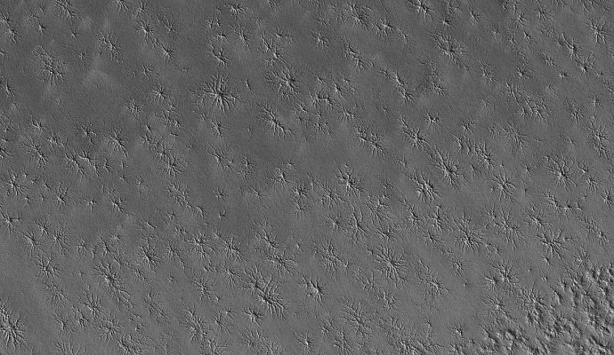 Spiderland (Original NASA/MGS/MSSS b/w Frame)
Caption originale:"This MGS-MOC image shows an area adjacent to the South Polar Residual Cap that hosts several intricate fracture networks. Each network consists of multiple fractures radiating from a central location. Their origin is not understood - some investigators have speculated that these are sites of release of carbon dioxide from beneath the ground, but this explanation seems inadequate to explain all attributes of the features. 
MOC images have shown that these features have not been changing from year to year during the course of the MGS mission".

Location near: 87,1° South Lat. and 234,1° West Long.
Image width: ~3 Km (~1,9 mi)  
Illumination from: upper left  
Season: Southern Summer
Parole chiave: Mars from orbit - South Polar Features - Spiders
