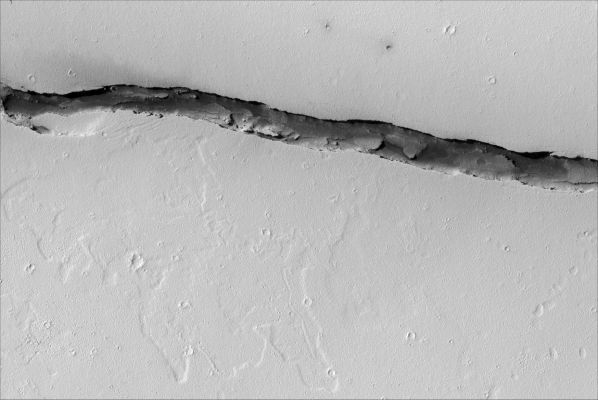 A long trough in Cerberus Fossae
The prominent trough in this image is a segment of the Cerberus Fossae rift system. In geological terminology the trough is known as a graben, or down-dropped region bounded by faults. In this location the graben is about 300 m wide and 90 m deep. Bright, dust-covered, cratered plains surround the graben, and darker sediments blanket much of its floor. Dunes that vary in size and spacing occur within the darker sediments, and their shapes suggest that the wind typically blows from east to west. Light-toned, angular boulders pepper the darker sediments. They have broken away from the rocky walls of the graben and tumbled downhill. Over time this mass wasting has caused the cliffs to retreat, widening the trough. The somewhat lighter patches of cratered terrain on the graben floor were once level with the surrounding plains, but have since been lowered by faulting. Over time they may become obscured or buried by the darker sediments. High-standing ridges - remnants of the former surface - cast jagged shadows on the floor of the graben that reveal the rugged nature of the landscape in this region of Mars. 


Parole chiave: Mars from orbit - Troughs