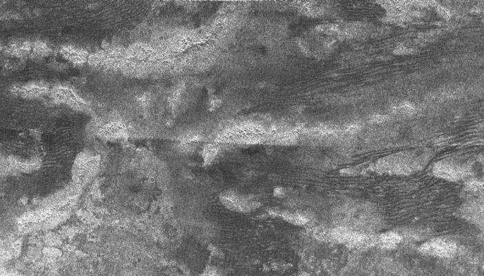 Possible Tectonic fractures on Titan
Original caption:"This synthetic aperture radar image of Titan was taken on Oct. 28, 2005, as the Cassini spacecraft flew by at a distance of 1.350 Km (about 840 miles). This was the first pass dedicated to radar and it was the fourth time Cassini's radar honed in on the smoggy moon. 
The bright, curving features are high-standing ridges, poking up above the plains of Titan. Some of the ridges extend for over 100 Km (roughly 60 miles). They are likely to be tectonic in origin, formed by deformation of Titan's icy crust. The low-lying terrain between the ridges is covered in dark streaks, which could be dunes formed by wind. The streaks, spaced 1 to 2 Km apart (0,6 to 1 mile), curve between patches of the bright terrain, which probably act as topographic barriers. 
This image is 400 Km (about 250 miles) across and 275 Km-wide (about 170 miles). It is located 8° South Latitude and 215° West Longitude".

Parole chiave: Saturn's Moons - Titan