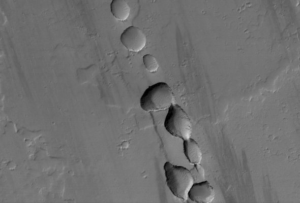 Collapse Pit-Chain near Tharsis Tholus (Original NASA/MGS/MSSS b/w Frame)
Caption NASA originale:"This MGS-MOC mage shows a portion of a Chain of Collapse Pits on a Lava and Dust-covered Plain, North/West of Tharsis Tholus —one of the many volcanic constructs in the Tharsis Region of Mars. 
Pit chains, such as this one, are associated with the collapse of surface materials into subsurface voids formed by faulting and expansion — or extension — of the bedrock".

Location near: 16,4° North Lat. and 92,6° West Long.
Image width: ~3 Km (~1,9 mi)  
Illumination from: lower left  
Season: Northern Winter
Parole chiave: Mars from orbit - Volcanic Features - Pit Chain