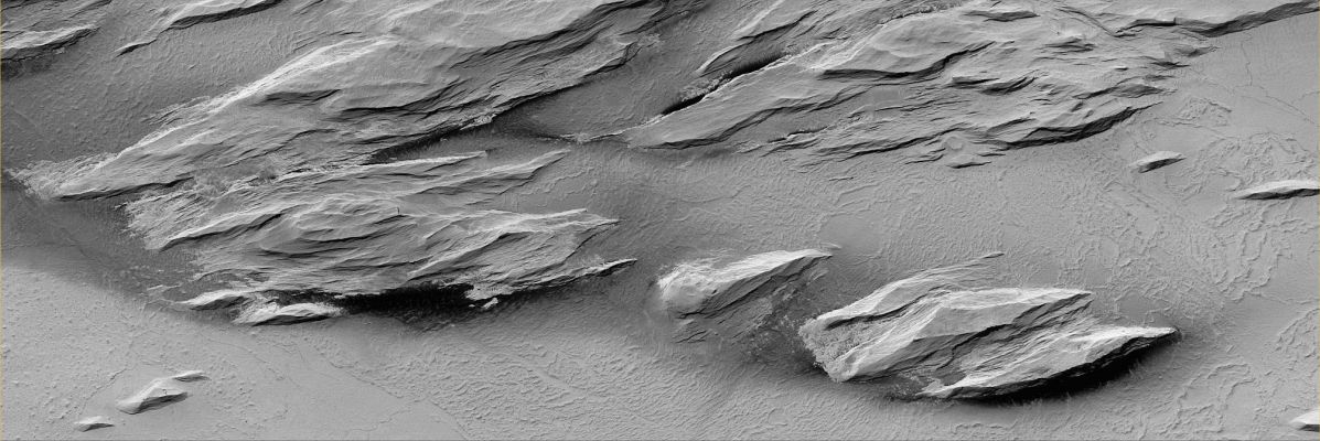 Streamlined Rocky Outcrops near Olympus Mons (Original NASA/MGS/MSSS b/w Frame)
Caption NASA originale:"This MGS-MOC image shows wind-eroded Outcrops overlying Lava Flow Surfaces located to the West of Olympus Mons. Outcrops with this appearance are also called Yardangs. Yardangs typically form in Sedimentary Rock or Volcanic Ash that contains some amount of Sand. The weathering of the Rock due to the Aeolian action cause the release of sand-sized particles from the Outcrops and, in time, such a form of erosion slowly shape the rock into the classic, inverted boat hull-like shapes of Yardangs". 

Location near: 13,2° North Lat. and 160,1° West Long.
Image width: ~3 Km (~1,9 mi)  
Illumination from: lower left  
Season: Northern Spring
Parole chiave: Mars from orbit - Volcanic Features - Rocky Outcrops