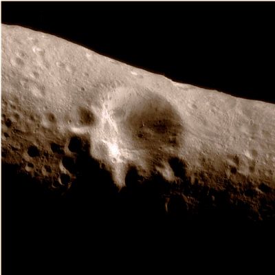Large Crater (natural colors; credits: Lunexit)
This image mosaic of the "Large Crater" at Eros' center was taken on March 3, 2000, during an optical navigation imaging sequence from a range of 127 miles (about 204 Km). This same area was imaged following orbit insertion at a range of approx. 210 miles (about 330 Km) on February 14th (Feb 14 G). 
This picture resolves features as small as 65 feet (20 meters) across compared to the resolution of 100 feet (30 meters) in the earlier image. The shadow cast by the boulder near the floor of the crater is now visible. The walls of the crater display some distinctive variations in their albedo or reflectivity. The upper part of the walls tend to be bright, while the lower portions of the walls and the crater floor show patches of darker or less reflective materials. These albedo patterns are also visible on other crater walls. To the right of the large crater, two sets of closely spaced orthogonal grooves are visible. 

(Mosaic of images 0127531846, 0127531908, 0127532094, 0127532156)
Parole chiave: Asteroids - 433-Eros