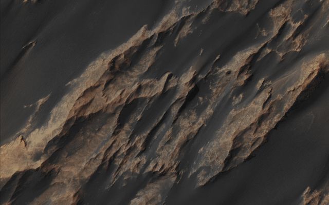 Features of Ophir Chasma (EDM - Absolute Natural Colors; credits for the additional process. and color.: Dr Paolo C. Fienga/Lunar Explorer Italia/Italian Planetary Foundation)
The really huge Landslides existing along the Walls of Ophir Chasma (which is nothing else but a deep Canyon located in the Coprates Quadrangle of Mars, at about 4° South Latitude and 72,5° West Longitude. It is approx. 317 km long and it was so named after a "Classical Albedo Feature") host a variety of Geologic Surfaces and Mineralogies. 
Some of them possess a variety of Hydrated Sulfate Minerals that formed, eons ago, in the presence of Partially Acidic Liquid Water. This NASA - Mars Reconnaissance Orbiter's Contextual (or "CTX", for short) Image, which is representing an ancient (possibly and approximately 3 Billion Years-old) Landslide, shows us the presence, within it, of 2 (two) very distinct Surface Albedoes, which, in fact, mark a Transition Zone from one Sulfate Mineralogy to another (a circumstance that proves beyod doubts the occurrence, in a far and distant past, of some remarkable variations in the evolution of the visible Surface).  
The Upper Slopes (such as the ones located towards the North) are light-toned, and this fact is due to the concurrent abundance of Hydrated Sulfate Minerals and Bright Surface Dust. On the other hand, the Surfaces that make up the Southern Portion of the Landslide, are darker in tone, and this is due to the greater abundance of Dark Sediment that, in time, formed "Strings of Sand Drifts" (extremely well visible in this Extra Detail Magnification). In addition to the above, the underlying Units of Bedrock consist of Darker Minerals that received a lesser hydration then the Northern ones, and this further circumstance implies the occurrence of a strong (and, perhaps, sudden) change in the Ancient Aqueous Environments that formed them. 

Mars Local Time: 14:52 (Early Afternoon)
Coord. (centered): 4,328° South Lat. and 288,657° East Long.
Spacecraft altitude: 271,0 Km (such as about 168,291 miles) 
Original image scale range: 27,1 cm/pixel (with 1 x 1 binning) so objects ~ 81 cm across are resolved
Map projected scale: 25 cm/pixel
Map projection: EQUIRECTANGULAR
Emission Angle: 6,3° 
Phase Angle: 52,7°
Solar Incidence Angle: 47° (meaning that the Sun was about 43° above the Local Horizon at the time the picture was taken)
Solar Longitude: 27,0° (Northern Spring - Southern Fall)
Credits: NASA/JPL/University of Arizona
Additional process. and coloring: Lunar Explorer Italia

This picture (which is an Original NASA - Original Mars Reconnaissance Orbiter - False Colors and NON-Map Projected sub-frame identified by the serial n. PSP_007535_1755-1) has been additionally processed, magnified, contrast enhanced, Gamma corrected, and then re-colorized in Absolute Natural Colors (such as the colors that a human eye would actually perceive if someone were onboard the NASA - Mars Reconnaissance Orbiter and then looked down, towards the Surface of Mars), by using an original technique created - and, in time, dramatically improved - by the Lunar Explorer Italia Team.
Parole chiave: Mars from orbit - Chasmas - Ophir Chasma