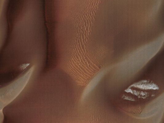 Proctor's Dunes (Possible Natural Colors; credits for the additional process. and color.: Dr Paolo C. Fienga - Lunexit Team)
This observation shows the edge of a dark Dunefield on the Floor of Proctor Crater, an about 150 Km (approx. 93 miles) diameter crater in the Southern Highlands of Mars.

This subimage is a close-up view of the dark dunes. These dunes are most likely composed of basaltic sand that has collected on the bottom of the crater. Superimposed on their surface are smaller secondary dunes which are commonly seen on terrestrial dunes of this size. Near the crests of the dark dunes are bright patches of frost. Dark spots within the frost patches are areas where defrosting is occurring.

Many smaller and brighter bed forms, most likely small dunes or granule ripples, cover the substrate between the larger dark dunes as well as most of the Floor of Proctor Crater. In many locations, large boulders are seen on the same surfaces as the bright bed forms. 
The dark dunes stratigraphically overlie the small bright bed forms indicating that the darker dunes formed more recently.

However in several areas, the dark dunes appear to influence the orientation of the small bright dunes, possibly by wind flowing around the larger dunes, suggesting that both dark and bright bed forms are coeval.
Parole chiave: Mars from orbit - Craters - Proctor Crater