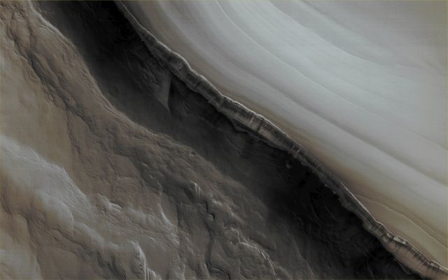 On the North Polar Scarp (EDM - Absolute Natural Colors; credits for the additional process. and color. Dr Paolo C. Fienga/Lunar Explorer Italia/Italian Planetary Foundation)
This image, taken by the NASA - Mars Reconnaissance Orbiter in the late November of the AD 2011, was acquired in order to monitor the effects on the North Polar Scarp of the so-called "Frost Avalanches" that occurred the year prior. HiRISE often re-images certain areas of Mars so to track those changes which, over time, might have occurred in some particularly interesting Regions and, in this case, the NASA People wanted to photograph the North Polar Scarp near the onset of the Martian Springtime, so to get a better understanding, among other things, of the number, extent and frequency of these Frost Avalanches; their possible causes (beside the thawing ---> the fact that Ice, Snow, or other frozen substances, start to become liquid, or just soft, as a result of warming) and the role that they have in the evolution of the North Poalr Scarp itself. 
It is a fact that, even though the HiRISE has captured the occurrence of many other Frost Avalanches in the past, their view never ceases to amaze, since it demonstrates (but we, as IPF, just like many other Researchers and Scientists all over the World, had no doubts about it) that there still are, even at present time, several Active Geologic and Atmospheric Processes which keep happening (or regular bases) on the Red Planet. And this one, in other words, is just "one of the many"...

Mars Local Time: 12:33 (Early Afternoon)
Coord. (centered): 84,995° North Lat. and 151,528° East Long.
Spacecraft altitude: 320,4 Km (such as about 200,2 miles) 
Original image scale range: 32,1 cm/pixel (with 1 x 1 binning) so objects ~ 96 cm across are resolved
Map projected scale: 25 cm/pixel
Map projection: POLAR STEREOGRAPHIC
Emission Angle: 0,5° 
Phase Angle: 71,1°
Solar Incidence Angle: 71° (meaning that the Sun was about 19° above the Local Horizon at the time the picture was taken)
Solar Longitude: 35,4° (Northern Spring - Southern Fall)
Credits: NASA/JPL/University of Arizona
Additional process. and coloring: Lunar Explorer Italia

This picture (which is a cropped and NON-Map Projected NASA - Original Mars Reconnaissance Orbiter CTX b/w frame, identified by the serial n. ESP_025010_2650) has been additionally processed and then colorized in Absolute Natural Colors (such as the colors that a human eye would actually perceive if someone were onboard the NASA - Mars Reconnaissance Orbiter and then looked down, towards the Surface of Mars), by using an original technique created - and, in time, dramatically improved - by the Lunar Explorer Italia Team.
Parole chiave: Mars from orbit - North Polar Regions - Scarp