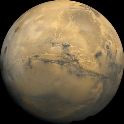 The Valles Marineris on Mars
Se tornassimo indietro nel tempo, diciamo di un tre miliardi di anni, e osservassimo Marte con un telescopio, con ogni probabilità vedremmo un pianeta completamente diverso da come esso ci appare oggi.
Più della metà della superficie planetaria, infatti, risulterebbe occupata da un immenso Oceano: l’Oceano Boreale (Oceanus Borealis).

La presenza di questo Oceano - profondo, probabilmente, fino ai 500-1500 metri, doveva provocare perturbazioni inerziali che necessitavano di essere bilanciate, affinché la rotazione di Marte fosse coerente, costante e continua.

Sulla Terra, la presenza dell’Oceano Pacifico genera una situazione analoga a quella del passato marziano. 

La condizione di "quasi-equilibrio rotazionale" è raggiunta sostanzialmente in questo modo: le masse crostali emerse a formare i continenti sono disposte in gran parte sull’emisfero opposto al Pacifico. La densità media delle rocce costituenti le terre emerse che si ergono fino a formare catene montuose e altipiani viene controbilanciata dalla somma della densità delle rocce oceaniche, più la densità della massa d’acqua ad esse sovrastante. 
Lo spessore della crosta oceanica è inferiore, in effetti, allo spessore della crosta continentale e questo è dovuto al valore della densità media delle rocce oceaniche (3,00 g/cm3) la quale è maggiore della densità media delle rocce continentali (2,7 g/cm3).

Il principio che governa le quote di giacitura di questi corpi rocciosi prende il nome di "Isostasia" e riguarda fondamentalmente il galleggiamento della crosta superficiale rigida sulla sottostante porzione di mantello astenosferico, caratterizzato da un comportamento fluido-plastico. L’equilibrio del sistema, comunque, non è totalmente raggiunto ed è per questo motivo che si riscontrano anomalie rotazionali quali la "Nutazione Libera di Eulero-Chandler", che consiste in oscillazioni dell’Asse di Rotazione Terrestre con un periodo di 430 giorni ed una  ampiezza di 0,1".

Se l’evaporazione dell’Idrosfera di Marte fu sufficientemente lenta, si può ragionevolmente supporre che i bilanciamenti isostatici avvennero gradualmente, attraverso milioni di anni e sfruttando - forse - una plasticità residua dei Corpi Geologici Marziani.

Se, al contrario, ciò che avvenne fu una rapida essiccazione (sulle cui cause, ad oggi, non ci è dato sapere nulla), è logico immaginare che i suddetti bilanciamenti avvennero in modo traumatico, attivando una geodinamica - per così dire - più aggressiva e caratterizzata dalla verificazione di eventi catastrofici concorrenti e/o rapidamente sequenziali (exx.: cicli di terremoti ad alta magnitudo; eventi magmatici - eruzioni - immensi dovuti alla risalita repentina verso la superficie del mantello fuso et sim.). 

Qualunque sia la Verità, noi possiamo dire che questo processo potrebbe spiegare, fra le altre cose, l’esistenza di estese depressioni tettoniche come, appunto, la Valles Marineris.

Potremmo, dunque (ed alla luce di quanto scritto fin’ora), affermare che la differenza di quota presente tra un Emisfero Marziano e l’altro potrebbe essere dovuta alla verificazione di un processo simile a quello terrestre? 

Ebbene la risposta è "si": è molto probabile.
Parole chiave: Planet Mars - The Valles Marineris