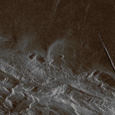 Danu Montes and Lakshmi Planum (possible Natural Colors; credits: Dr Paolo C. Fienga - Lunexit Team)
Southwest Lakshmi Planum is bounded on the South by the Danu Montes. 

Lakshmi Planum is an elevated plateau plain that is bounded on all sides by mountain chains. Here, the Danu Mountains have an angular fractured appearance. Chasms slice diagonally across the mountains in the lower left (South-West) corner of the image. Because of the steep slopes and the local relief of the mountains of several kilometers (2-3 miles, these fault-bounded troughs appear to zig-zag through the mountains when, in fact, they are probably straight if viewed from above. 

The radar view provides a perspective that would place the viewer's eye to the right, 27° above the Horizon. Thus, slopes facing to the right can be seen completely, though dark, and slopes facing away to the left appear shortened, often seen only as thin bright lines. In the center of the image is a low volcanic dome (approx. 20 Km - about 12 miles - in diameter). 
This type of volcanic feature frequently occurs on the low plains. This dome on the edge of Lakshmi is deformed and faulted where it has been affected by the forces that created the Danu mountains. 

The image is approx. 75 Km (about 46 miles) on a side. The center is at 60° North Latitude and 324,5° East Longitude.
Parole chiave: Venus from orbit - Lakshmi Planum Regio