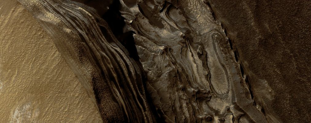 North Polar Layered Deposits in Head Scarp of Chasma Boreale (EDM - Natural Colors; credits: Lunexit)
This EDM shows the NPLD at top and darker materials at bottom exposed in a Scarp at the head of Chasma Boreale, a large canyon eroded into the Layered Deposits.

The Polar Layered Deposits appear of a brown/reddish color because of dust mixed within them, but they are ice-rich as indicated by previous observations. The water ice in the Layered Deposits is probably responsible for the pattern of fractures seen near the top of the scarp.

The darker material below the Layered Deposits may have been deposited as sand dunes, as indicated by the cross-bedding (truncation of curved lines) seen near the middle of the Scarp. 
It appears that brighter, ice-rich layers were deposited between the dark dunes in places. 

Exposures such as these are useful in understanding the recent climate variations that are likely recorded in the Polar Layered Deposits.
Parole chiave: Mars from orbit - North Polar Regions - NPLD