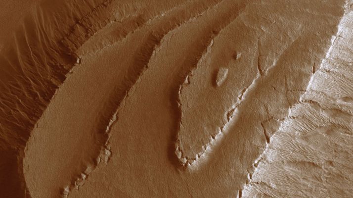 Layers in Spallanzani Crater (extra-detail mgnf)
The layers within Spallanzani Crater are eroding in a stair-stepped pattern. 
Each layer appears as a sequence of a broad flat area or plateau, which drops off abruptly down to the next flat surface (see this extra-detail mgnf). 

This stair-stepped pattern suggests that the layers have discreet boundaries that may be the result of differing compositions, time of deposition, or both. Near, but not at the edge of each plateau, the material is fracturing into polygonal plates or blocks that tilt downward away from the plateau center. 
Parole chiave: Mars from orbit - Craters - Spallanzani Crater
