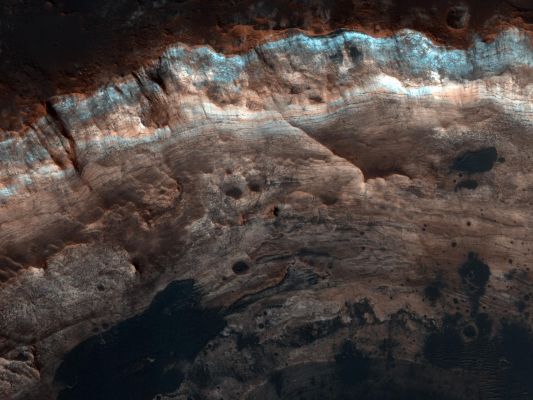 Unnamed Crater with Layers near Mawrth Vallis (Enhanced Natural Colors; credits: NASA/JPL-Caltech/University of Arizona)
This image covers part of an Unnamed Impact Crater roughly 4 Km (approx. 2,5 miles) in diameter; the upper portion of the picture shows a one Km segment of the Crater's Inner Wall and Rim.
The Surface outside the Crater is relatively dark, while the Inner Wall of the Crater exposes lighter, Layered Bedrock of diverse colors. A few dark patches on the Crater Wall have small Dunes or Ripples on their surfaces, and are likely Pits filled with Dark Sand. This Crater provides a window into the Sub-Surface of Mars, revealing Layered Sedimentary Deposits.

Just about 30 Km (approx. 18,6 miles) to the East of this Crater lies Mawrth Vallis, an ancient Channel that may have been carved by catastrophic Floods. 
In Layered Deposits surrounding Mawrth Vallis, the orbiting spectrometers OMEGA (on Mars Express) and CRISM (on MRO) have detected Phyllosilicate (such as Clay) minerals, which must have formed in the presence of water. 

In this Region on Mars, the colors of the Layers seen by HiRISE often correlate with distinct water-bearing minerals observed by CRISM, so the color diversity seen here may reflect a dynamic environment at this location on early Mars.

Note: the color in these images is enhanced; it is not as it would normally appear to the human eye.
Parole chiave: Mars from orbit - Craters - Unnamed Crater with Layered Bedrock
