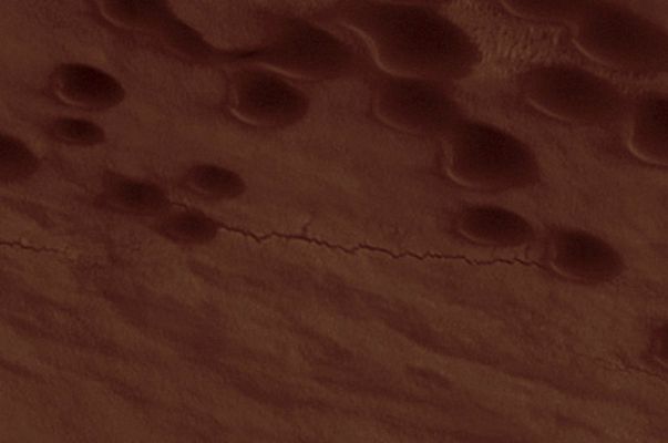 Dunes and other Surface Features in Chasma Boreale (edm n. 2 - natural colors; credits: Lunexit)
Le dune che vedete in questo dettaglio extramagnificato del panorama relativo alla Regione di Chasma Boreale SEMBRANO essere collegate da una frattura longitudinale, semi-irregolare ed a bordi frastagliati. Questa "frattura", se sovrasaturiamo l'immagine ed operiamo una ulteriore magnificazione, mostra delle leggere differenze di colore e di albedo e, alla fine, pare assomigliare davvero molto ad un canale di drenaggio (una sorta di fiumiciattolo, per dirla semplicemente). 
Rilievi similari li abbiamo già incontrati su Titano e, se per i drainage channels della Luna Nebbiosa non paiono esserci più dubbi sul fatto che un qualche tipo di liquido scorra nel loro letto, per quanto attiene Marte ancora tutto tace.

In realtà, il fatto che questa specie di "frattura" superficiale possa essere un piccolo canale (che si inserisce in un ampio reticolo di canali - osservate il ctx frame per capire il contesto di riferimento) e che all'interno di esso scorra qualcosa, è pura speculazione; ma che la "frattura" (rectius: il network di fratture) sia oltremodo recente, è un fatto (basta osservare il dettaglio magnificato con una minima attenzione per capirlo).

La NASA, nel commentare questo frame, non si sofferma su queste "curiose" fratture del suolo e non ci offre alcuna idea/spiegazione delle stesse.

Peccato.
Parole chiave: Mars from orbit - North Polar Regions - Chasma Boreale - Controversial Feature