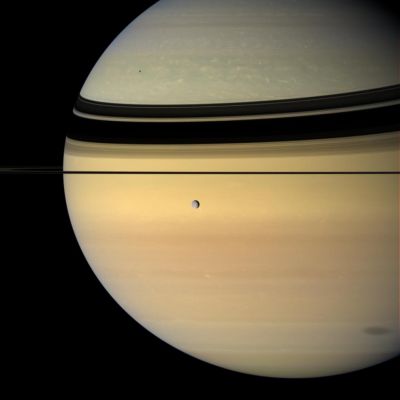 Shadows on the Giant
Like a silvery pearl, an icy moon crosses the face of Saturn, while 2 of its siblings cast shadows onto the Planet. 
Rhea hangs in the foreground. Near upper left on Saturn is the small shadow of Mimas. Near lower right is the penumbral shadow of Japetus - the part of the moon's shadow where Japetus does not completely block the Sun. 

This view looks toward the unilluminated side of the Rings from less than 1° above the Ring-Plane. The Rings' shadows drape across the Northern Hemisphere. Images taken using red, green and blue spectral filters were combined to create this natural color view. The images were obtained with the Cassini spacecraft wide-angle camera on June 15, 2007, at a distance of approx. 1,2 MKM (such as about 744.000 miles) from Rhea and 1,7 MKM (1,1 MMs) from Saturn. 
Image scale is roughly 71 Km (about 44 miles) per pixel on Rhea and 103 Km (about 64 miles) on Saturn.
Parole chiave: Saturn's Rings and Rhea