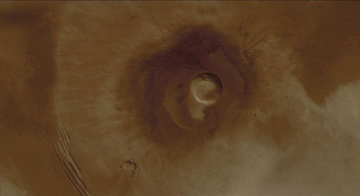 Pavonis Mons (Enhanced and Saturated Natural Colors; credits for the additional process. and color.: Dr Paolo C. Fienga - Lunexit Team)
Caption NASA originale:"This Mars Global Surveyor (MGS) Mars Orbiter Camera (MOC) wide angle color composite image, obtained in December 2003, shows the middle of the three Tharsis Montes, Pavonis Mons. 
This is a broad shield volcano - similar to the volcanoes of Hawaii - located on the Martian Equator at approx. 113° West. The Volcano Summit is near 14 Km (~8,7 mi) above the Martian Datum (such as 0 elevation); the central caldera (crater near center of image) is about 45 Km (~28 mi.) across and about 4,5 Km (~2.8 mi.) deep. Sunlight illuminates the scene from the lower left".  
Parole chiave: Mars from orbit - Volcanoes - Pavonis Mons